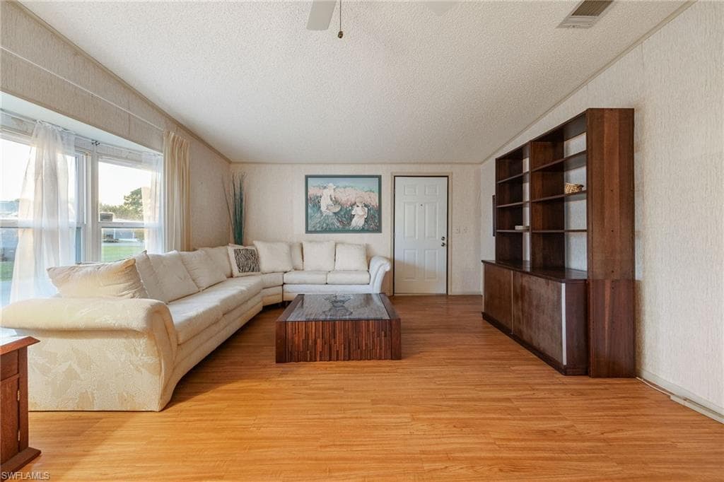 Living room with light wood-style flooring, a textured ceiling, wallpapered walls, and ceiling fan