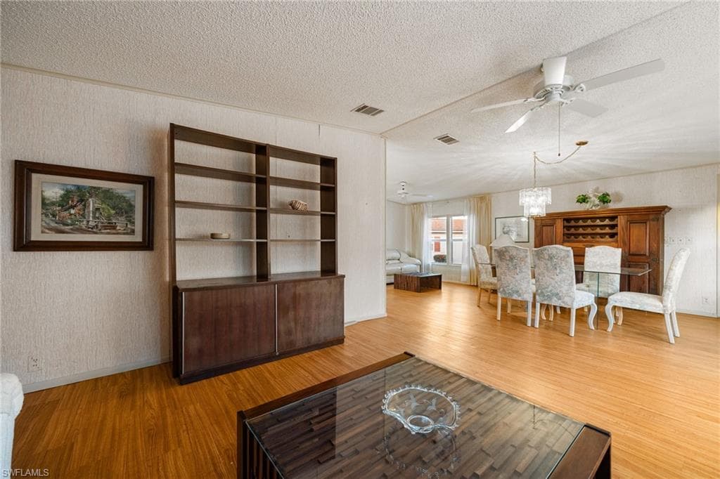 Living room with wood finished floors, a ceiling fan, a chandelier, and a textured ceiling