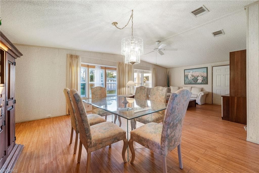 Dining area featuring a textured ceiling, light wood finished floors, a ceiling fan, wallpapered walls, and a chandelier