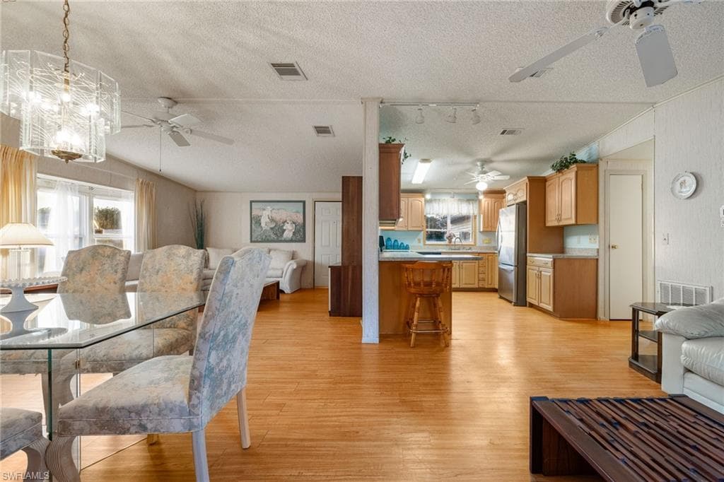 Dining area featuring a textured ceiling, a ceiling fan, light wood-style flooring, track lighting, and a chandelier
