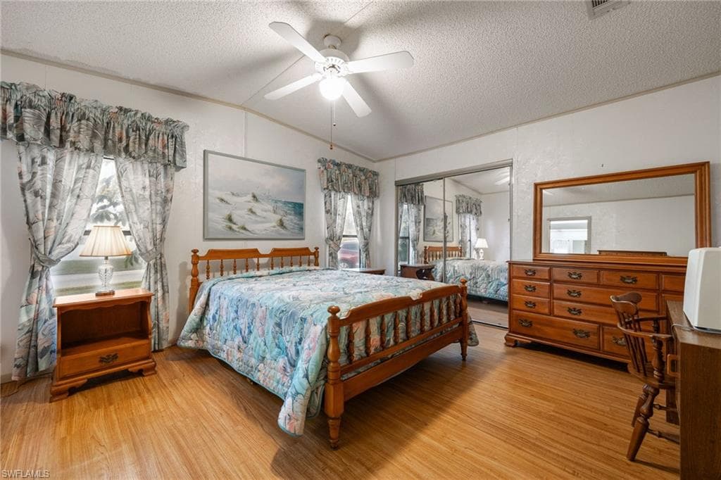 Bedroom with a closet, lofted ceiling, light wood finished floors, a textured ceiling, and a ceiling fan