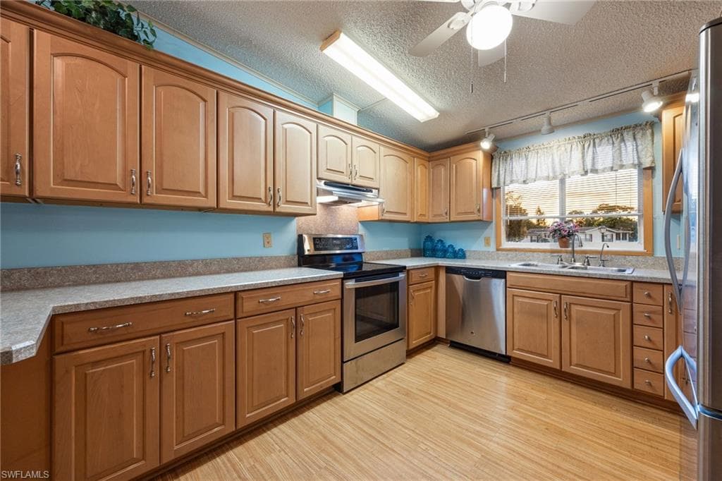 Kitchen featuring a textured ceiling, stainless steel appliances, rail lighting, light wood-style floors, and a ceiling fan