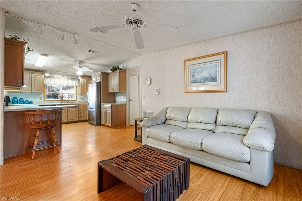 Living area with a textured ceiling, light wood finished floors, and track lighting