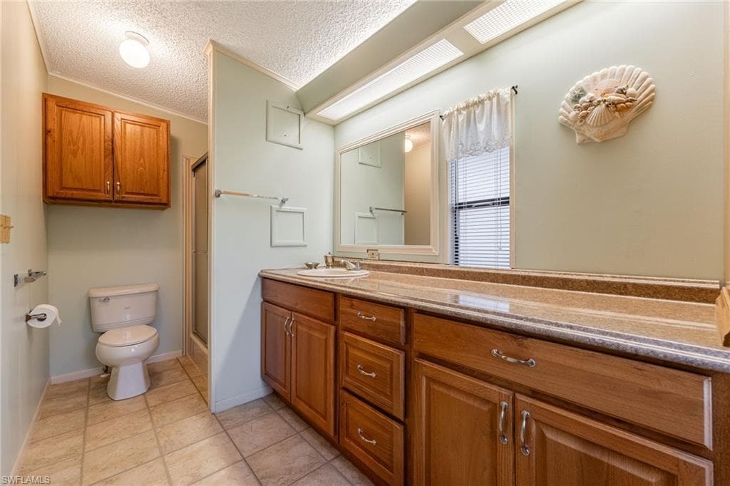 Full bathroom featuring a shower stall, a textured ceiling, vanity, crown molding, and light tile patterned floors