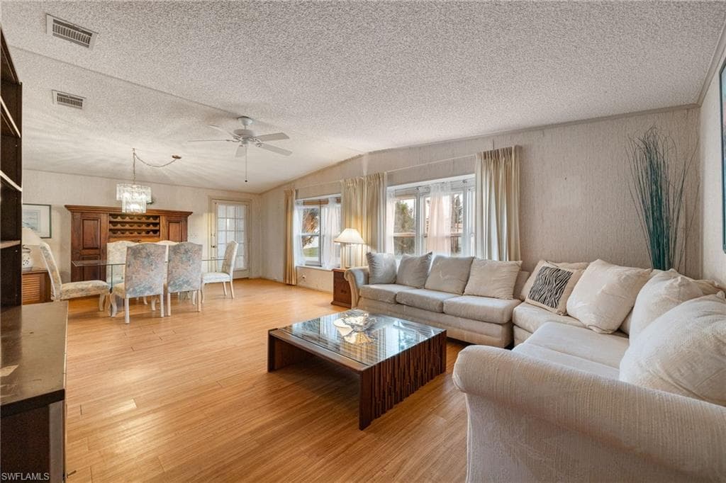 Living room featuring light wood-style flooring, a textured ceiling, lofted ceiling, and ceiling fan