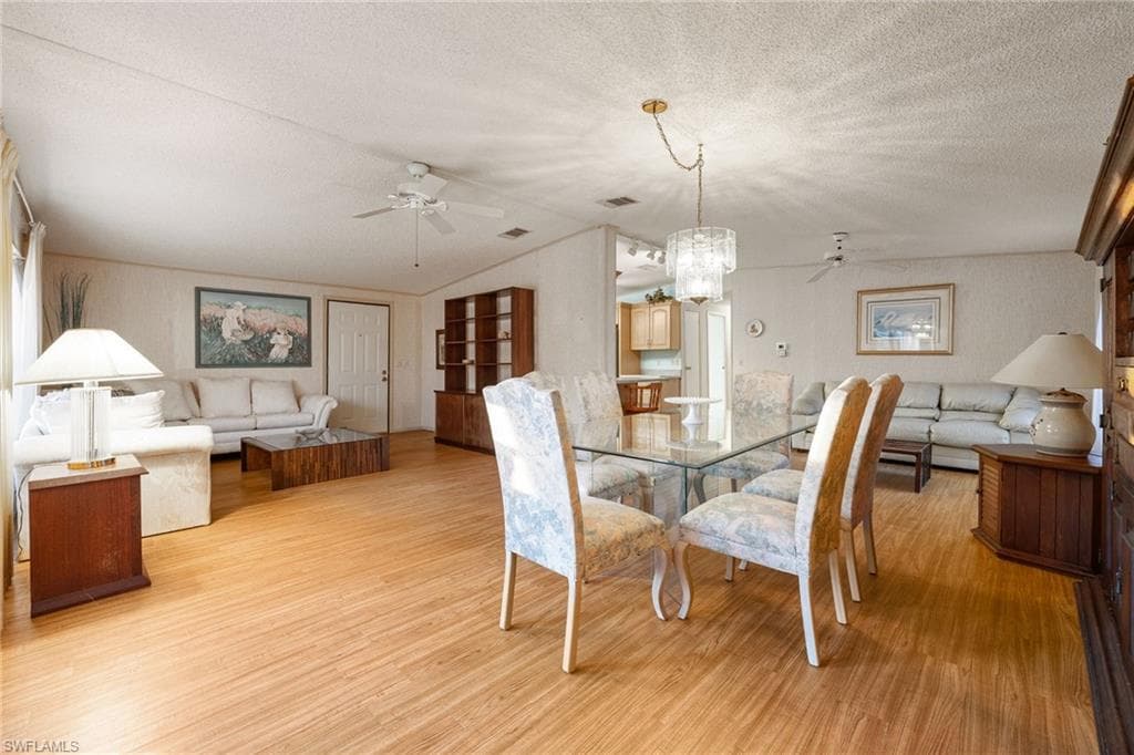 Dining space featuring ceiling fan, lofted ceiling, light wood-type flooring, a textured ceiling, and a chandelier