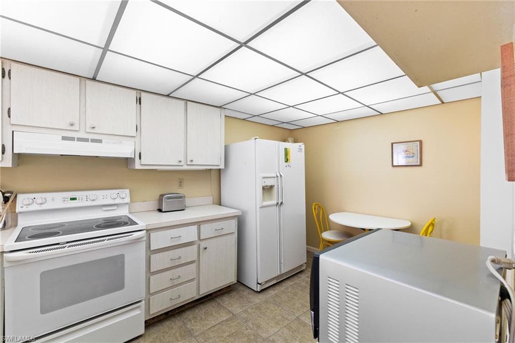 Kitchen featuring white appliances, light countertops, under cabinet range hood, and light tile patterned floors