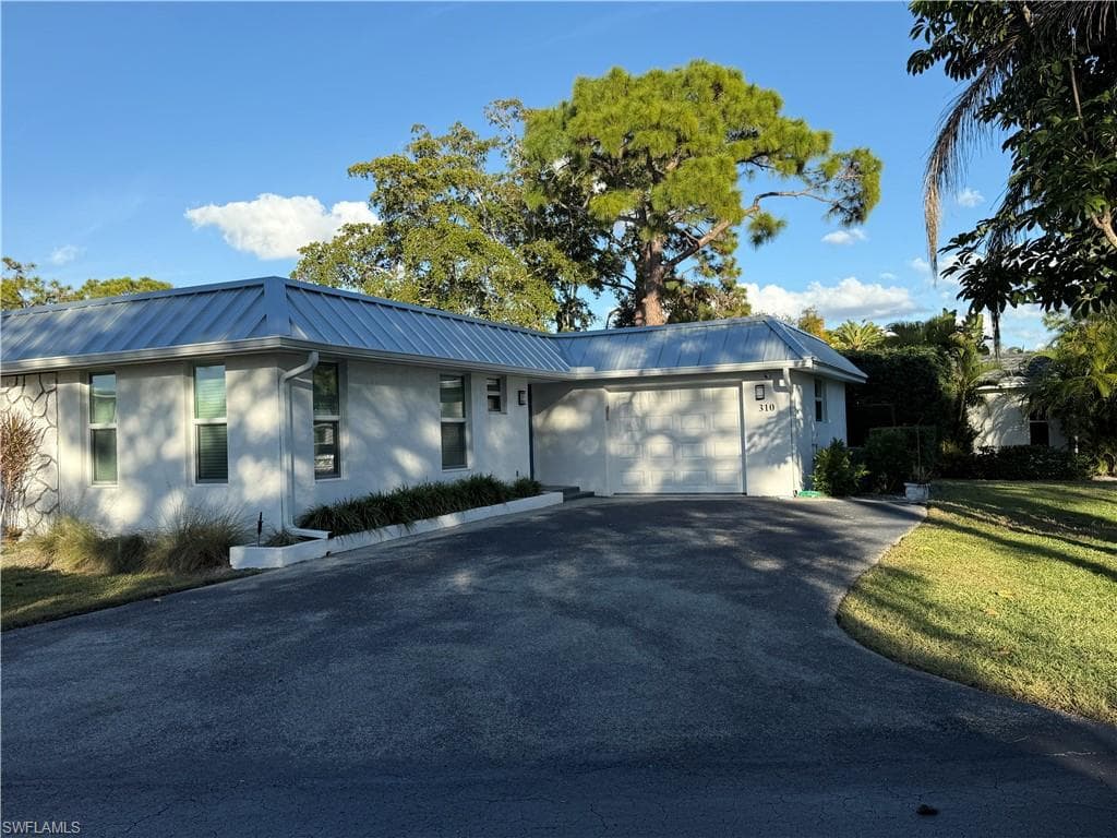 Ranch-style house featuring driveway, a metal roof, a garage, and stucco siding