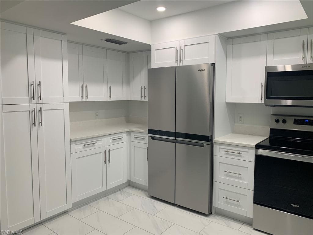Kitchen with appliances with stainless steel finishes, white cabinetry, light marble finish floors, light stone counters, and recessed lighting