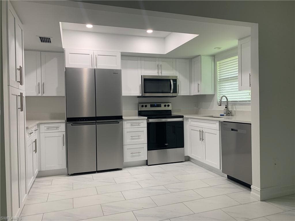 Kitchen with appliances with stainless steel finishes, white cabinetry, light marble finish flooring, recessed lighting, and light stone countertops