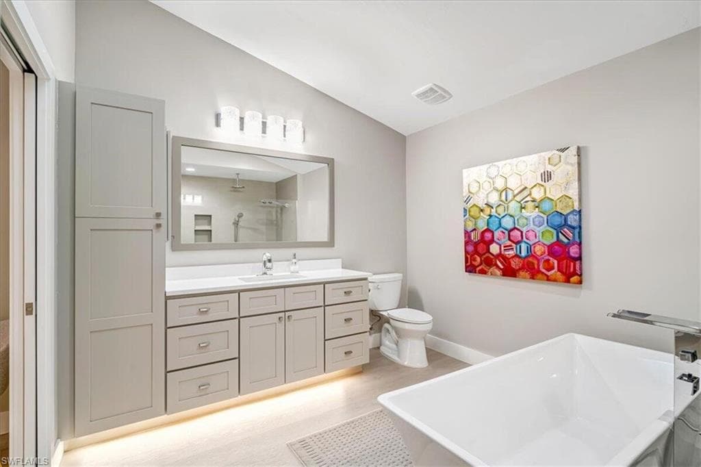 Full bath featuring vanity, vaulted ceiling, a freestanding bath, a shower, and light wood finished floors