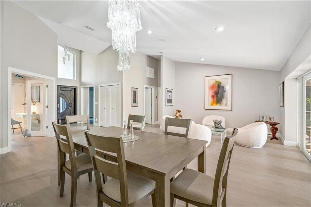 Dining room featuring high vaulted ceiling, light wood-style flooring, recessed lighting, and a chandelier