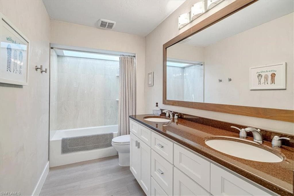 Bathroom featuring double vanity, shower / tub combo with curtain, and light wood finished floors