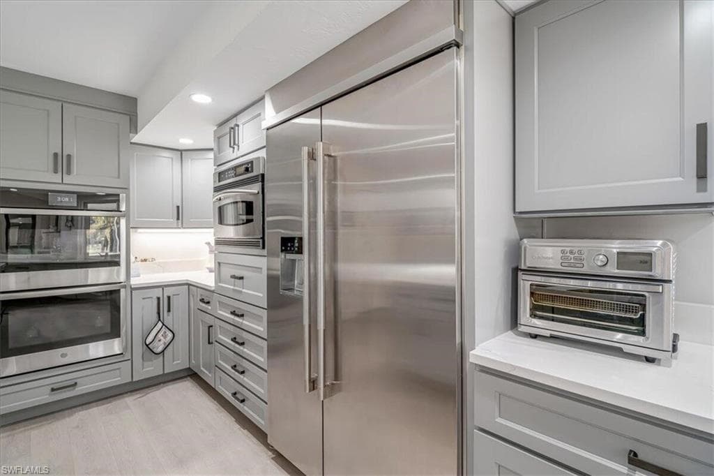 Kitchen featuring gray cabinetry, appliances with stainless steel finishes, recessed lighting, light wood-style flooring, and light stone counters