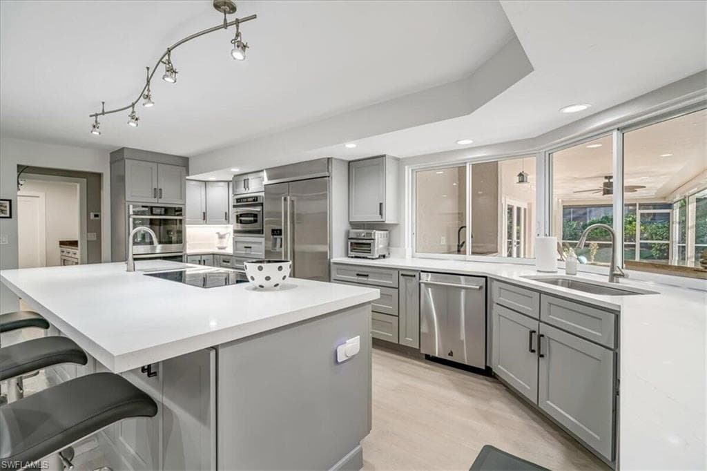 Kitchen with gray cabinetry, a kitchen island with sink, a breakfast bar area, light wood finished floors, and appliances with stainless steel finishes