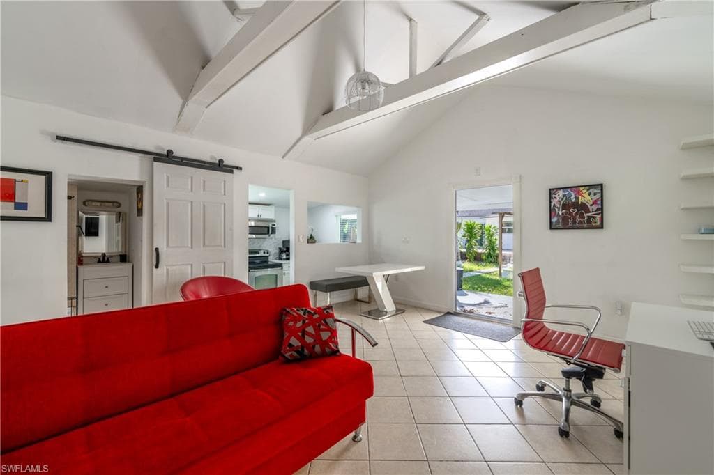 Office area featuring beamed ceiling, a barn door, light tile patterned floors, and high vaulted ceiling