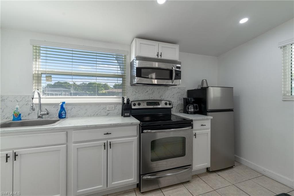 Kitchen with appliances with stainless steel finishes, white cabinets, tasteful backsplash, light tile patterned flooring, and plenty of natural light