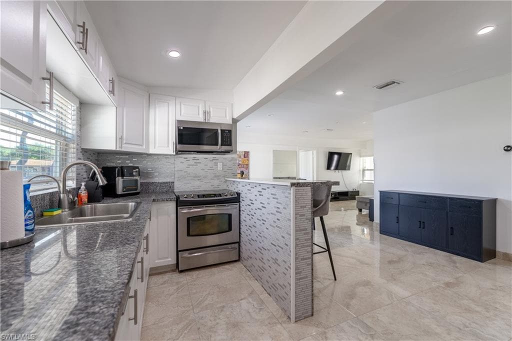 Kitchen with a breakfast bar, appliances with stainless steel finishes, decorative backsplash, dark stone countertops, and white cabinets