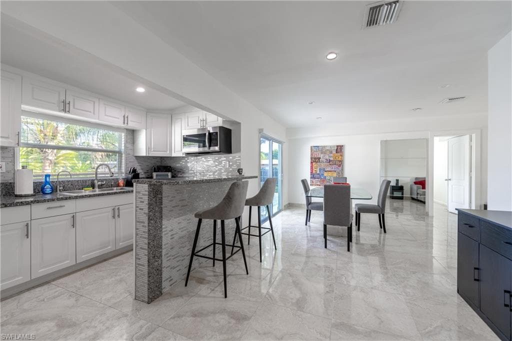 Kitchen featuring tasteful backsplash, dark stone countertops, stainless steel microwave, white cabinetry, and recessed lighting
