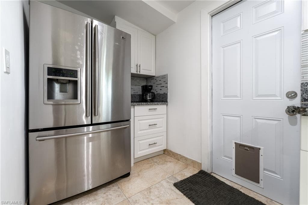 Kitchen with stainless steel refrigerator with ice dispenser, white cabinets, decorative backsplash, dark stone countertops, and light tile patterned floors