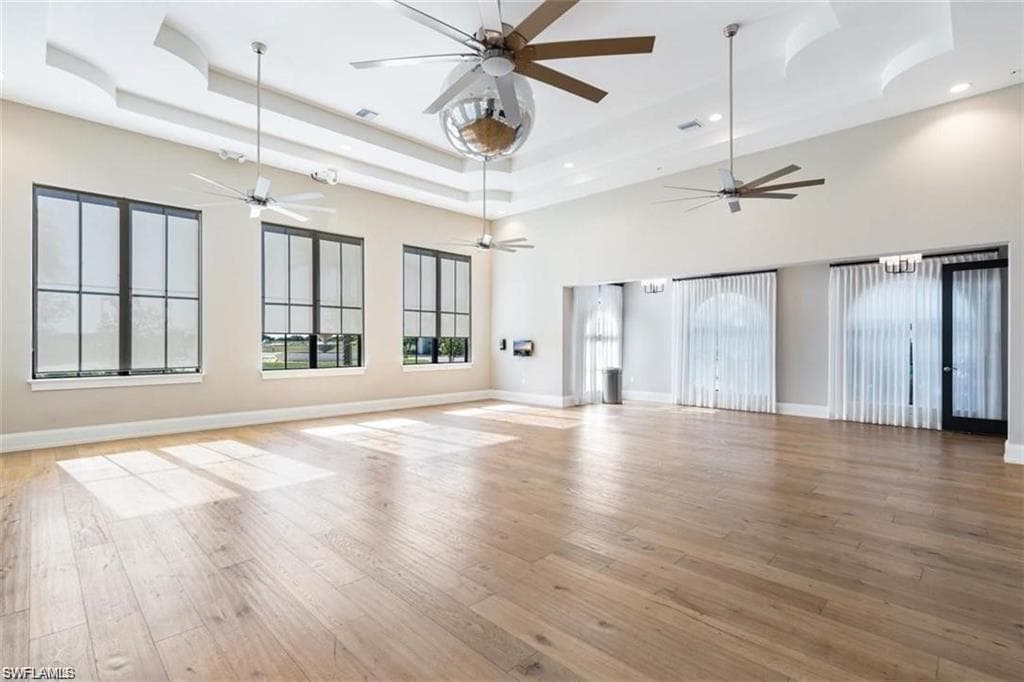 Unfurnished living room with a raised ceiling, light wood finished floors, and a towering ceiling