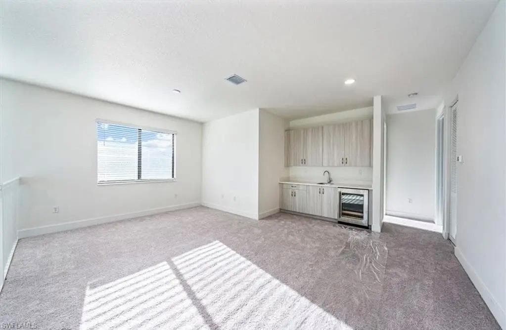 Unfurnished living room featuring light colored carpet, beverage cooler, wet bar, and recessed lighting