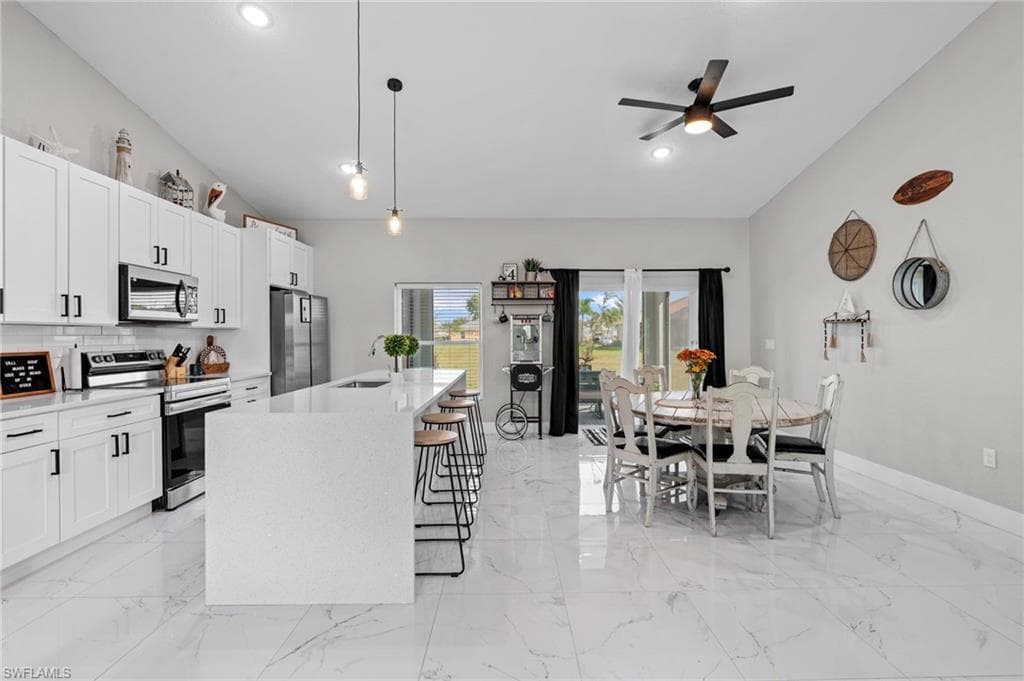 Kitchen featuring stainless steel appliances, hanging light fixtures, light stone countertops, a center island with sink, and white cabinetry