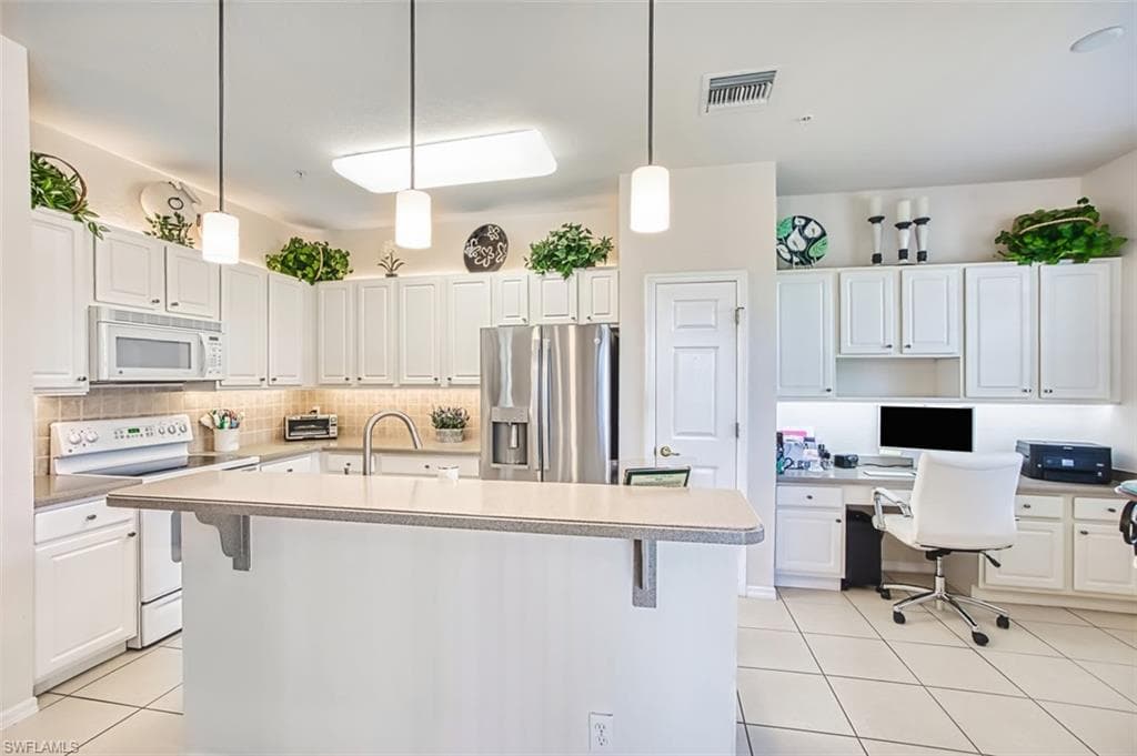 Kitchen with light tile patterned flooring, white appliances, built in study area, white cabinetry, and pendant lighting