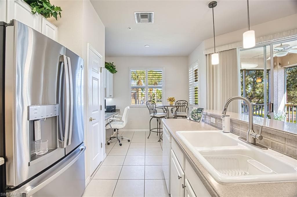 Kitchen with stainless steel refrigerator with ice dispenser, white cabinets, hanging light fixtures, light tile patterned floors, and light countertops