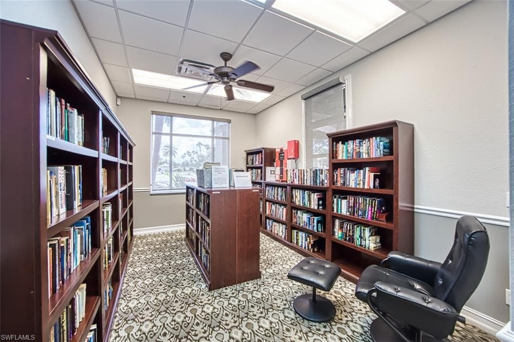 Sitting room featuring a drop ceiling, wall of books, and a ceiling fan