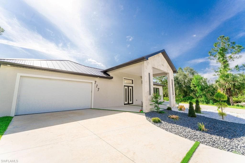 View of front of house with stucco siding, concrete driveway, a metal roof, and a garage