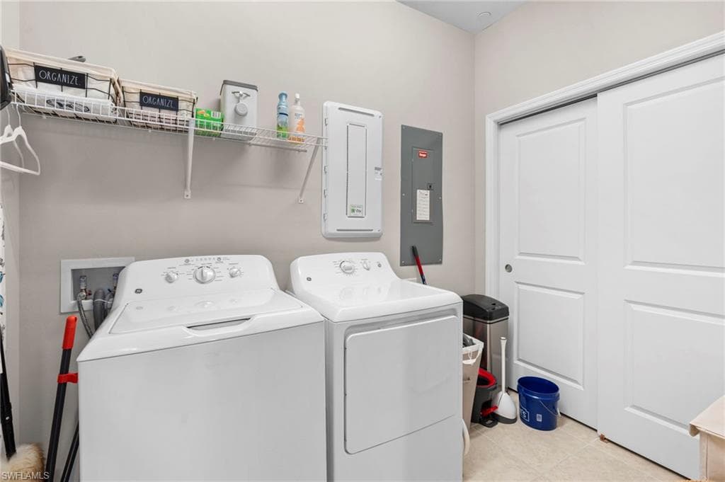 Washroom with electric panel, light tile patterned floors, and washer and dryer