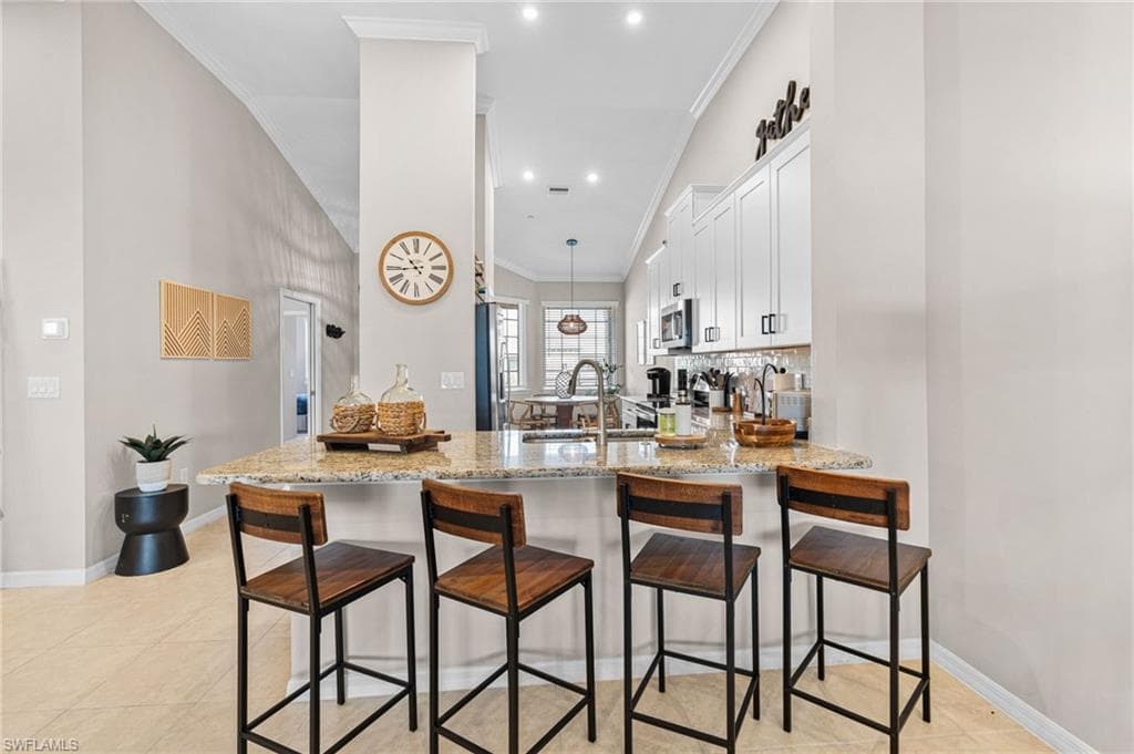 Kitchen with a breakfast bar area, light stone counters, white cabinetry, decorative light fixtures, and a peninsula