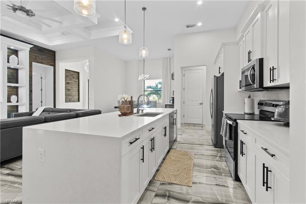Kitchen with white cabinets, stainless steel appliances, open floor plan, pendant lighting, and a kitchen island with sink