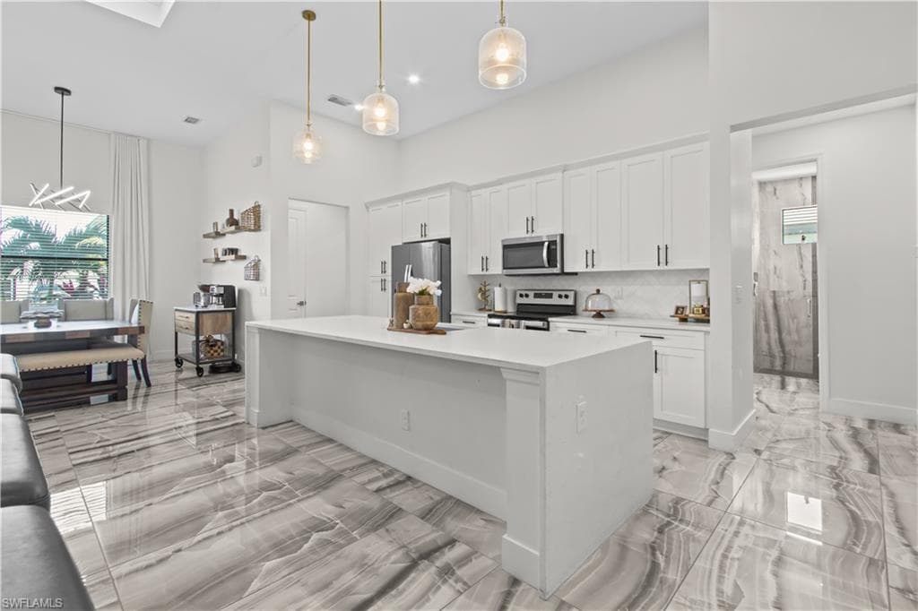 Kitchen featuring light marble finish flooring, white cabinetry, stainless steel appliances, healthy amount of natural light, and a towering ceiling