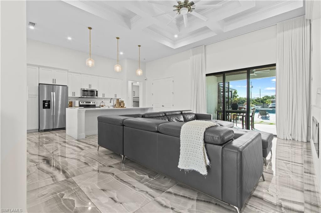 Living room with light marble finish floors, a towering ceiling, coffered ceiling, beam ceiling, and ceiling fan