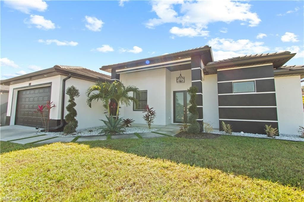 View of front of home featuring stucco siding, a garage, and a front lawn