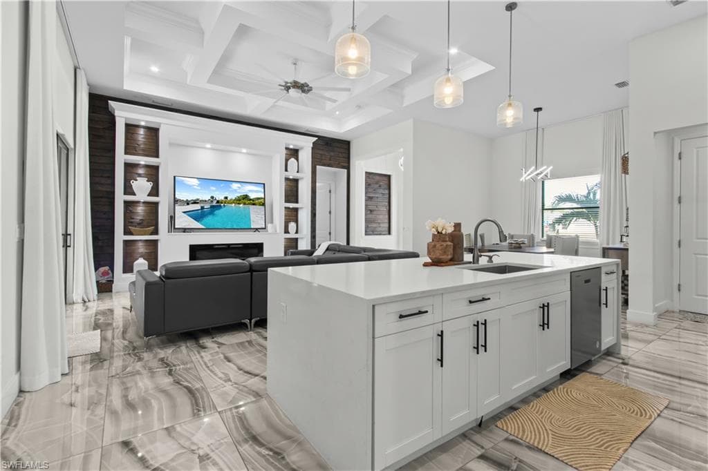Kitchen with decorative light fixtures, white cabinets, ceiling fan, light stone counters, and an island with sink