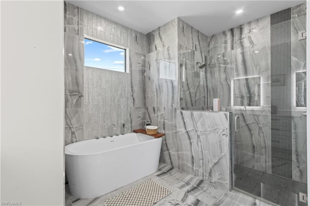 Bathroom with tile walls, a freestanding bath, a marble finish shower, and recessed lighting
