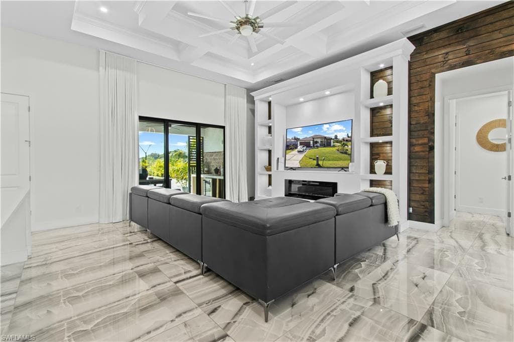 Living room featuring a glass covered fireplace, coffered ceiling, light marble finish flooring, built in shelves, and beam ceiling