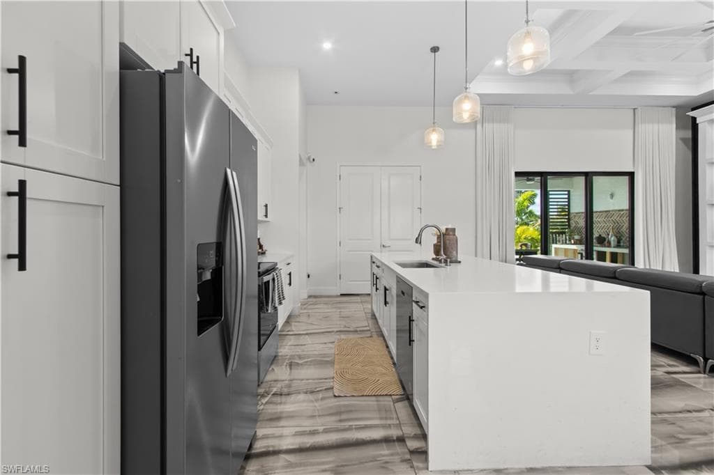 Kitchen with stainless steel appliances, white cabinets, beam ceiling, pendant lighting, and light stone countertops