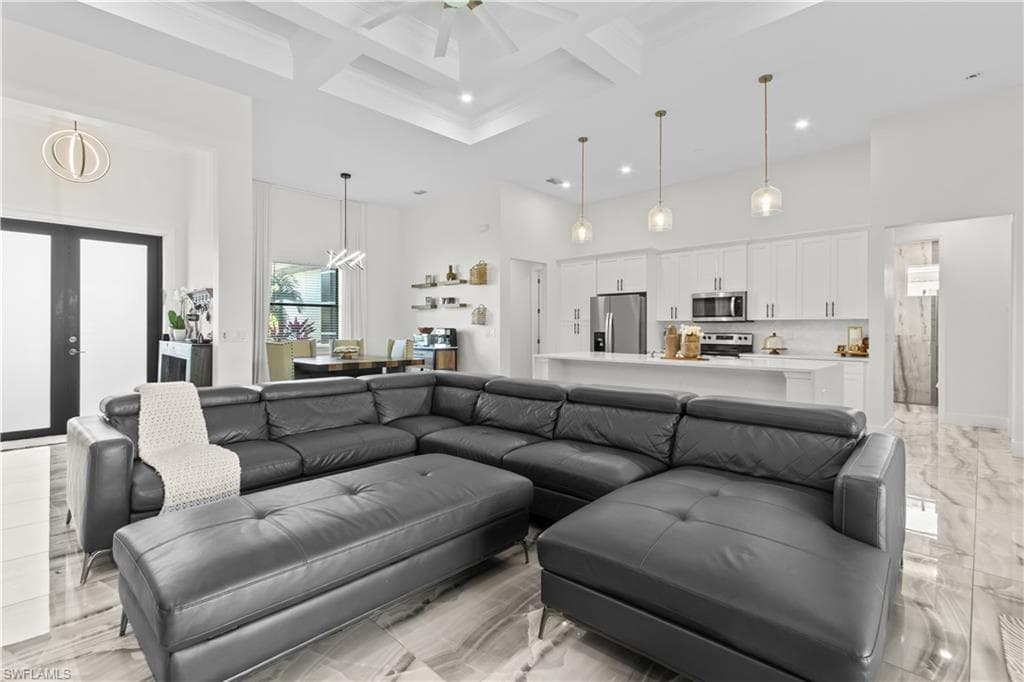 Living area with coffered ceiling, a high ceiling, beam ceiling, light marble finish floors, and a chandelier