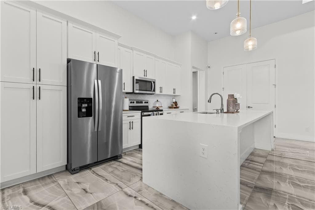 Kitchen with appliances with stainless steel finishes, decorative backsplash, hanging light fixtures, light stone countertops, and white cabinetry