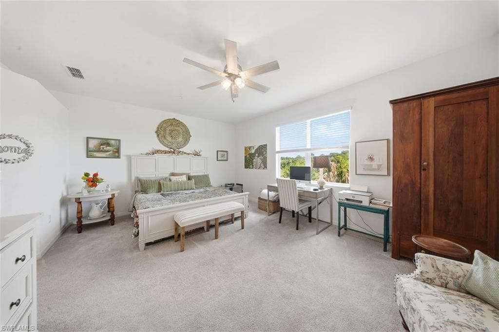 Bedroom featuring light colored carpet, a ceiling fan, and an office area