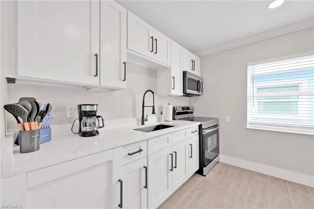 Kitchen featuring stainless steel appliances, white cabinets, light stone counters, ornamental molding, and wood finish floors