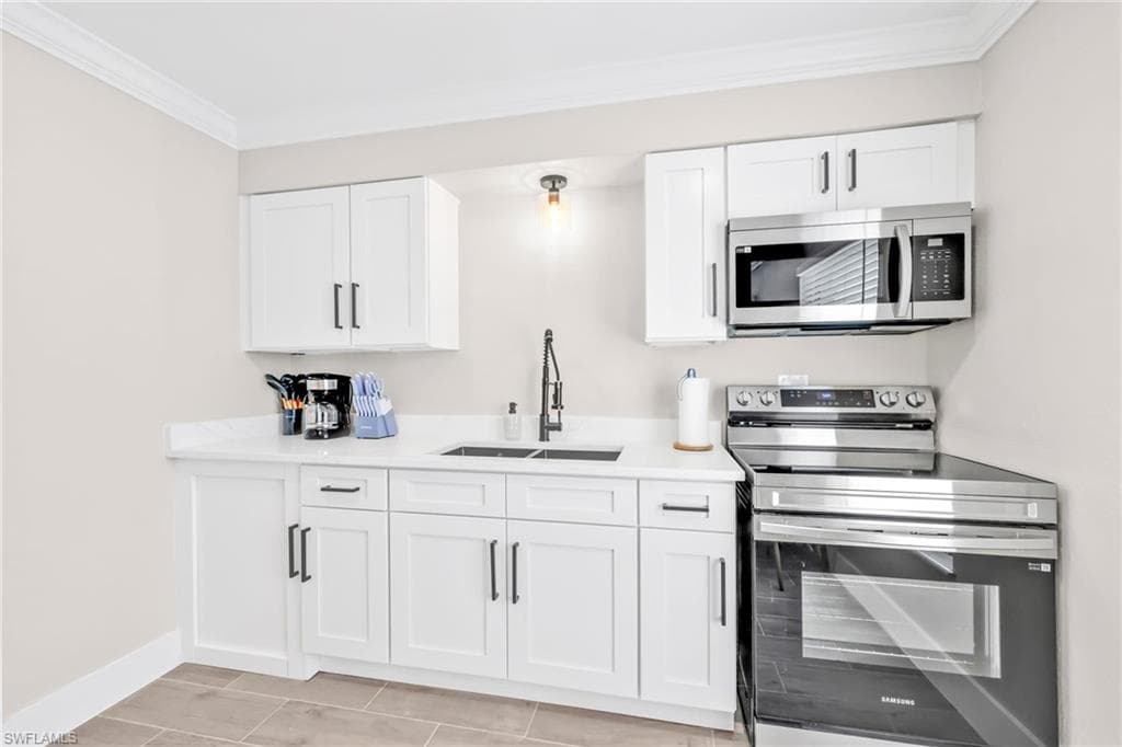 Kitchen with stainless steel appliances, white cabinetry, crown molding, and light stone counters