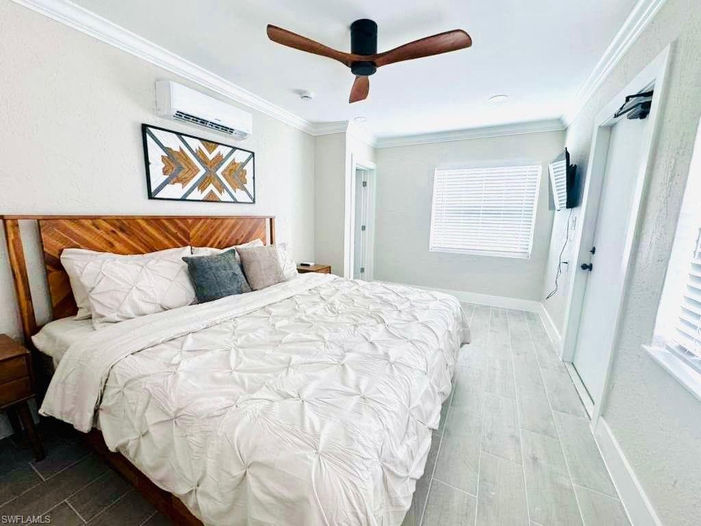 Bedroom featuring ornamental molding, wood tiled floors, a ceiling fan, and a wall unit AC