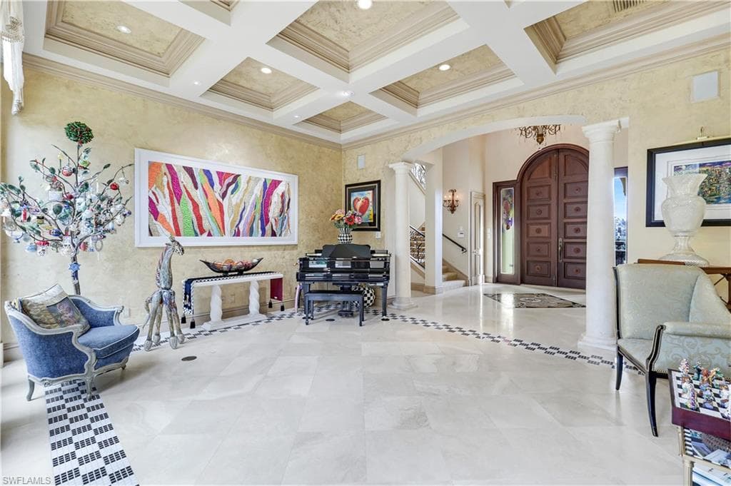 Living room with ornate columns, arched walkways, coffered ceiling, ornamental molding, and beamed ceiling