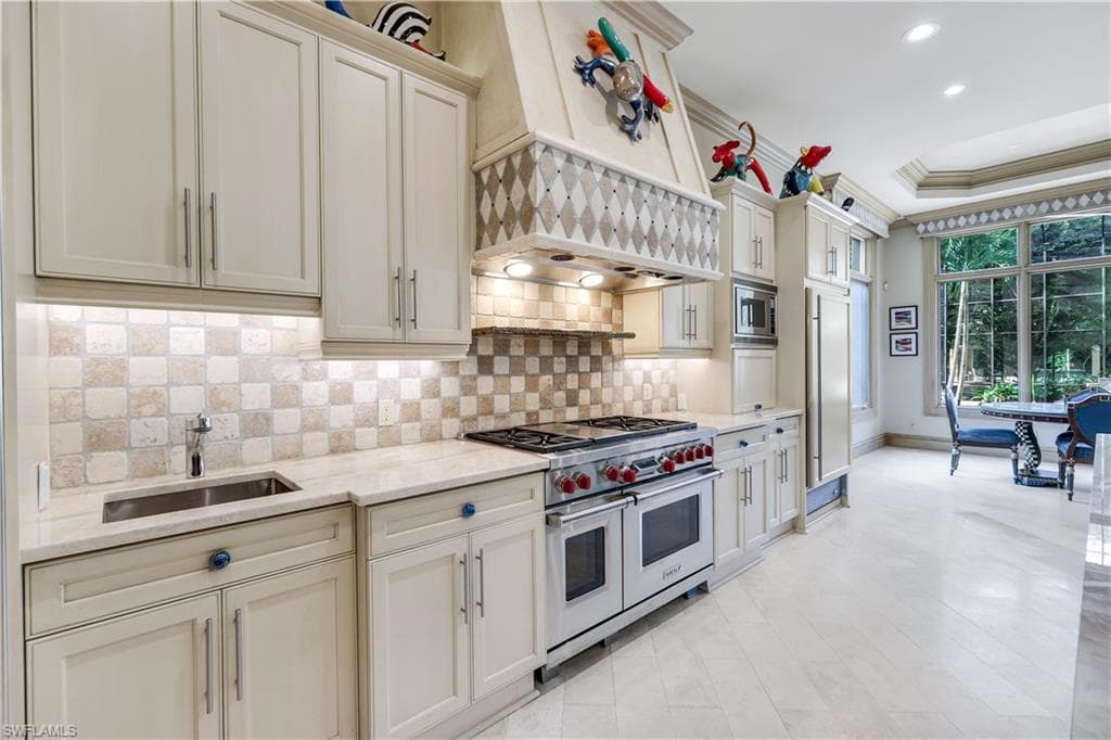 Kitchen with built in appliances, premium range hood, ornamental molding, light stone counters, and a raised ceiling