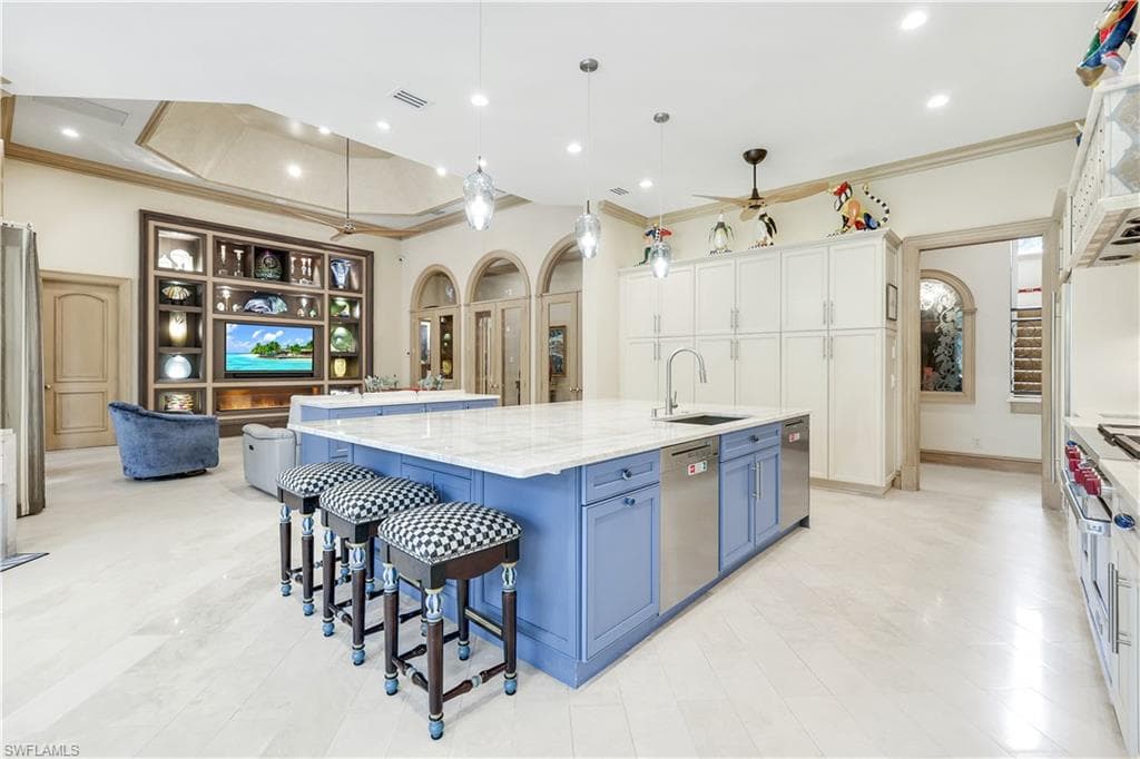 Kitchen featuring a kitchen bar, blue cabinetry, hanging light fixtures, a large island with sink, and crown molding